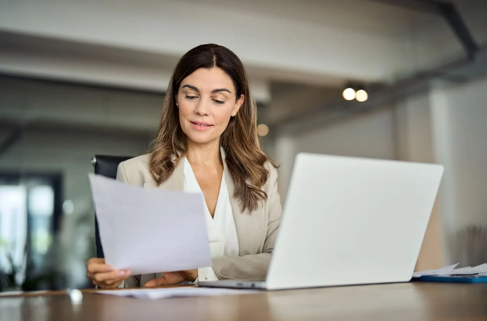 Woman reviewing documents beside a laptop at a desk